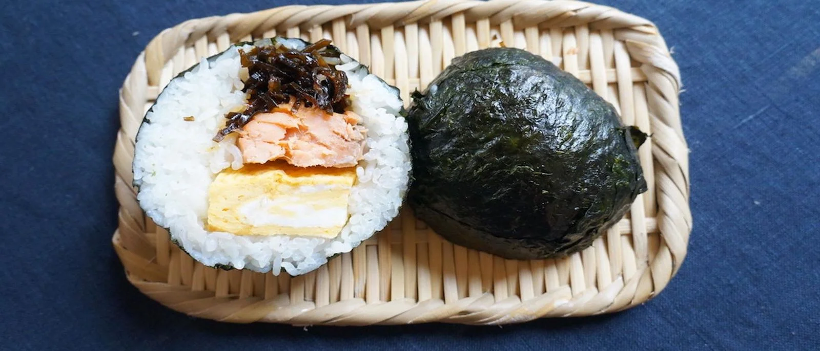 A bakudan onigiri cut in half to show salmon, rolled omelette and kombu inside, next to a whole one
